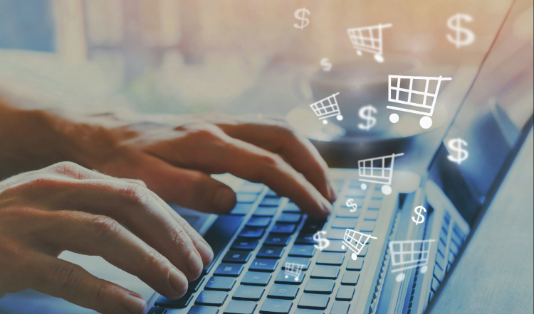 A person's hands are posied on a keyboard as shopping carts and dollar signs appear above the screen.