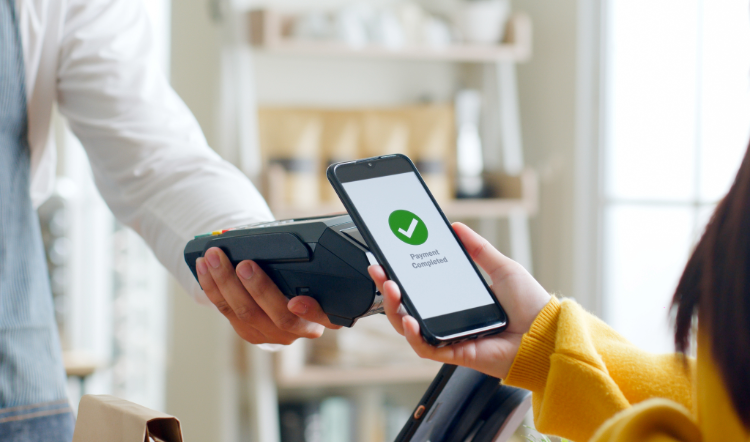 Someone holds a phone over a payment terminal to use a mobile wallet for a purchase.
